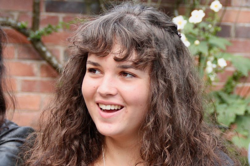 A photo of a smiling young white woman with curly brown hair.